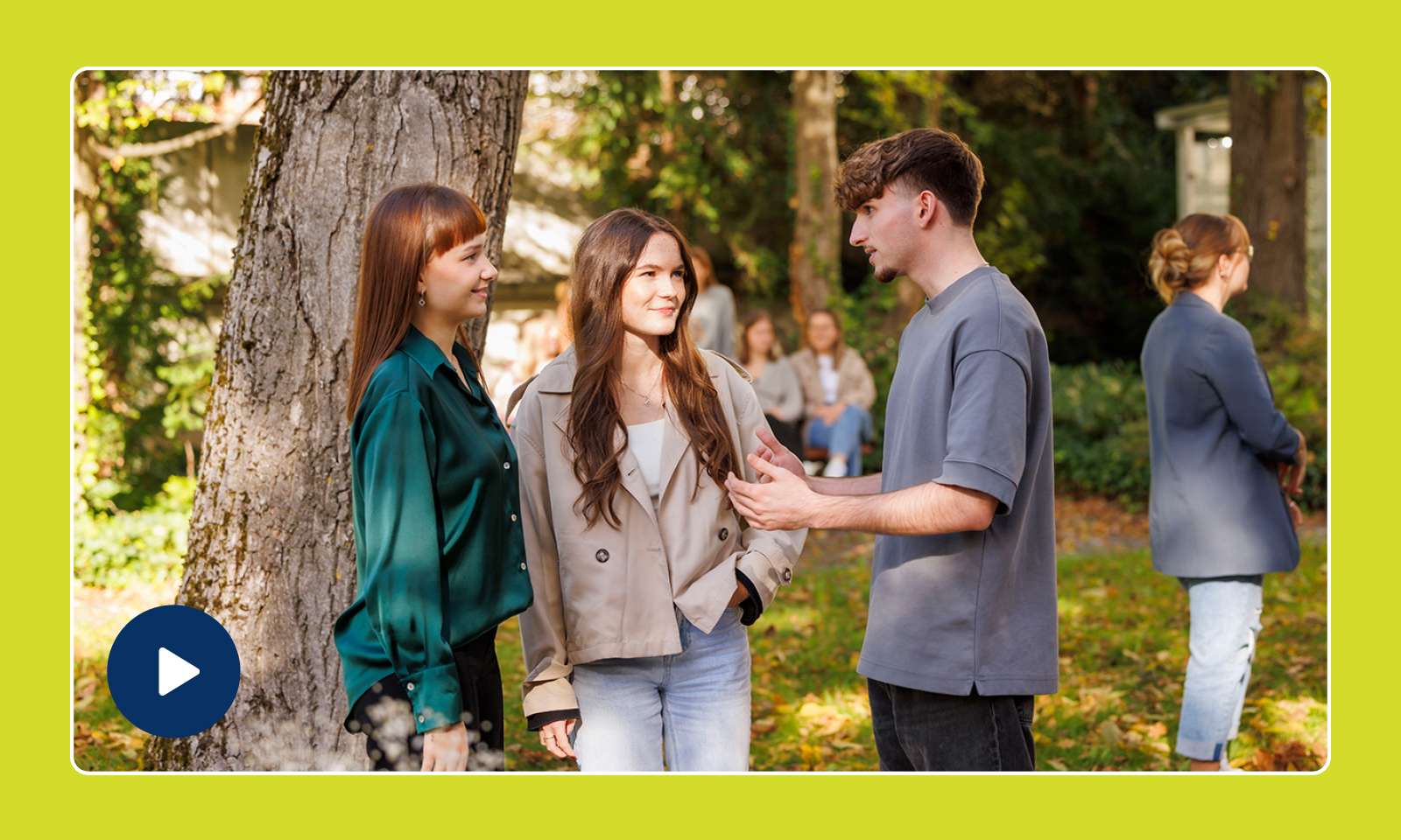 Drei junge Erwachsene stehen unter einem Baum und unterhalten sich lächelnd, während sich im Hintergrund weitere Personen befinden.