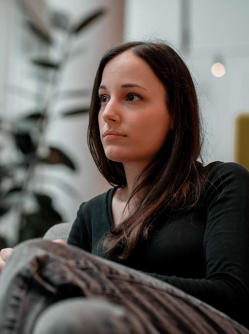 Sarah schaut sitzend nachdenklich in die Ferne. Im Hintergrund ist der Coworking-Space zu sehen.